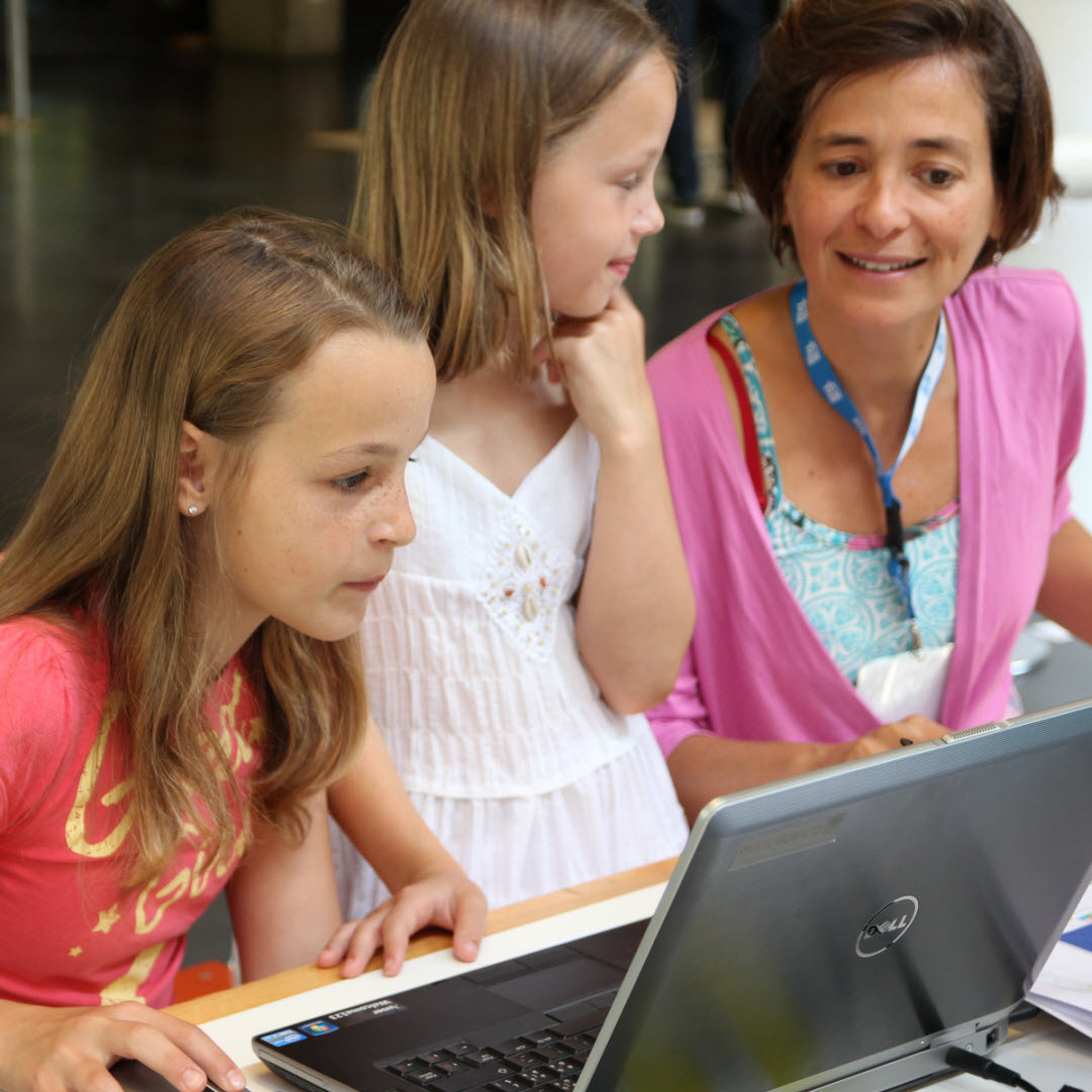 Foto: ein Mädchen programmiert, zweites Mädchen 
                        schaut lächeld die Trainerin an