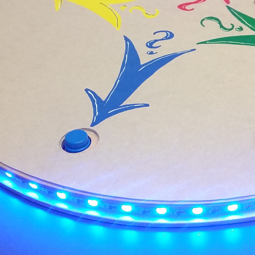 Foto einer Leuchtscheibe: blau leuchtende LEDs und blaue 
                        Taste mit blauem Pfeil auf Buzzer-Spielfeld